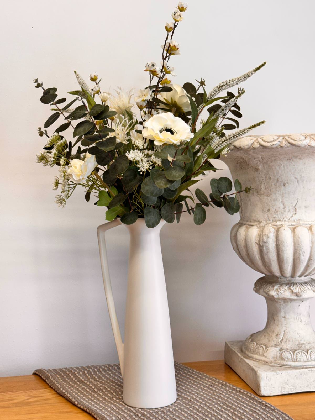 A striking artificial arrangement with Blossom, Thistle, Veronica, Trachelium, and Anemones, styled in a tall white ceramic vase.