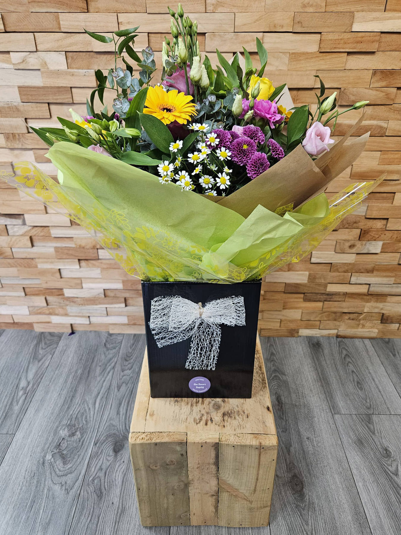 Brighten any day with Vivid Charm – a fresh bouquet of yellow roses, gerbera, daisies, lisianthus, and alstroemeria. Hand-tied, delivered locally.